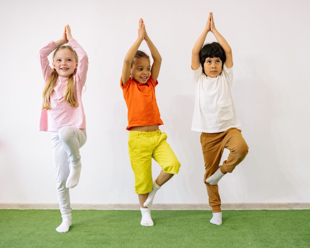 Kinder üben in einem hellen Raum gemeinsam Yoga auf ihren Matten.