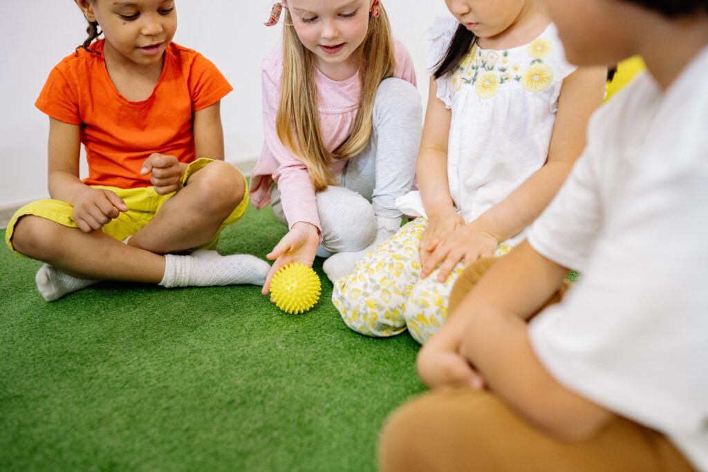 Eine Kursleiterin zeigt einer Kindergruppe eine Yogahaltung, die Kinder machen konzentriert mit.